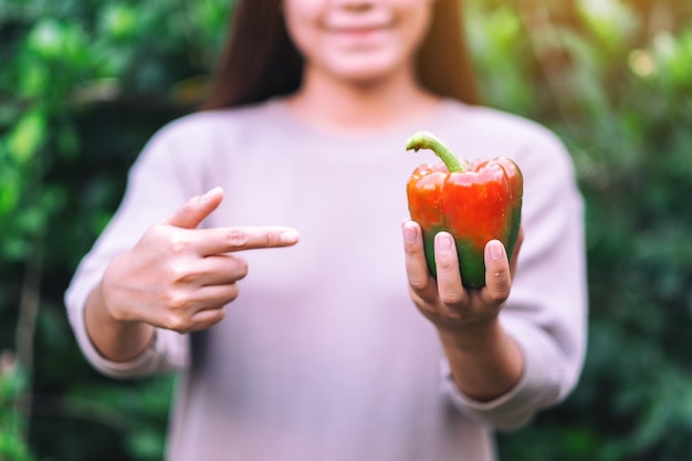 Une femme tenant et pointant du doigt un poivron frais