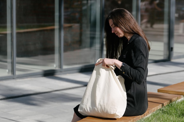 Femme tenant un sac écologique textile blanc sur fond de ville urbaine Concept d'écologie ou de protection de l'environnement Sac écologique blanc pour maquette