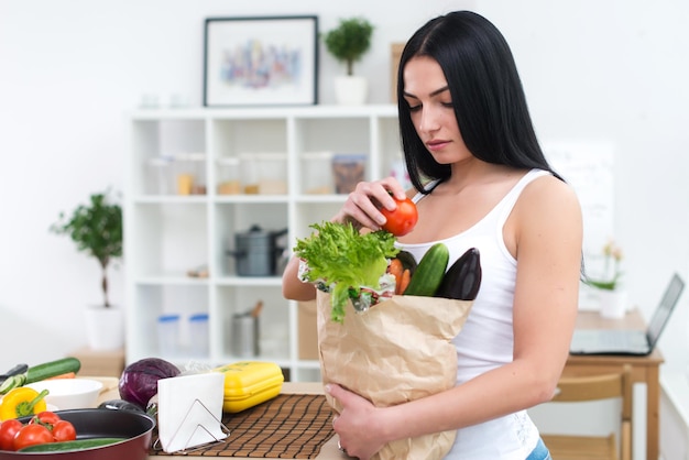 Femme tenant un sac en papier avec une épicerie fraîche regardant attentivement en choisissant des ingrédients pour un régime alimentaire sain