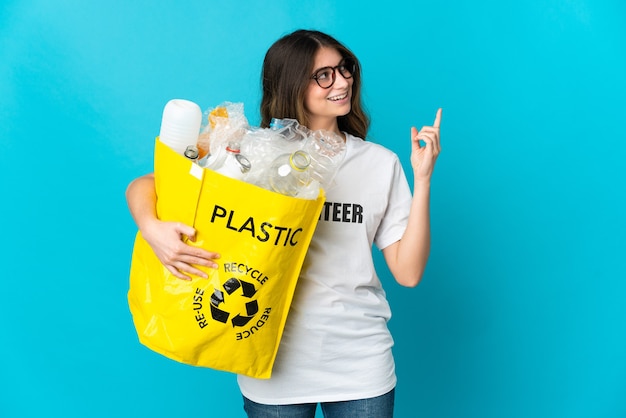 Femme tenant un sac plein de bouteilles à recycler isolé sur bleu pointant vers le haut une excellente idée