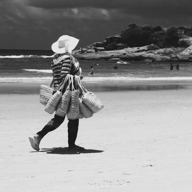 Femme tenant des sacs en marchant sur la plage contre le ciel