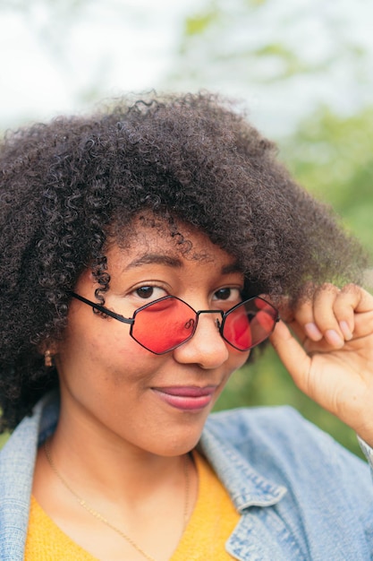 Femme tenant ses lunettes de soleil et regardant la caméra en se tenant debout dans le parc