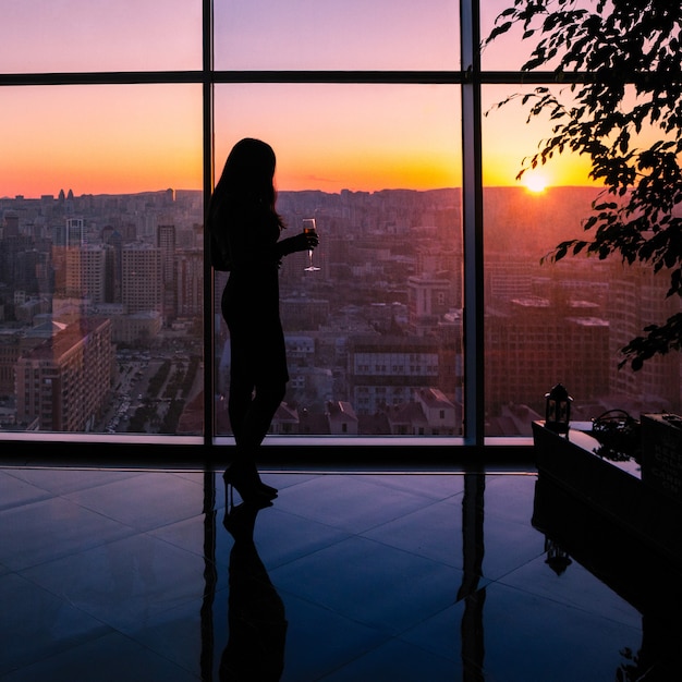 Femme tenant la silhouette de verre à champagne, regarde la vue sur la ville