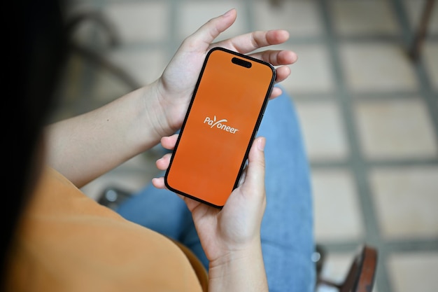 Une femme tenant un smartphone avec le logo Payoneer à l'écran