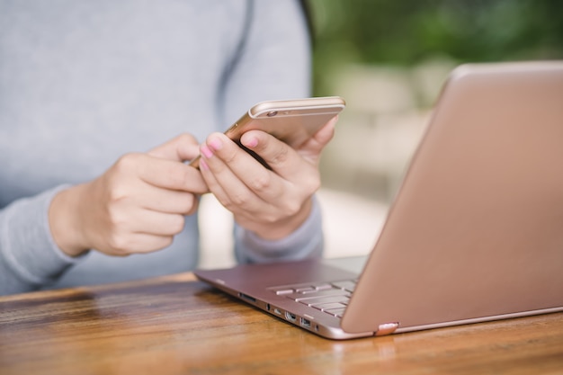 Femme tenant un smartphone recevant un message avec confirmation de transaction sur ordinateur portable