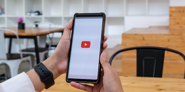 Femme tenant un smartphone avec service vidéo YouTube à l'écran.