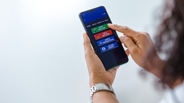 Femme tenant des smartphones et utilisant le toucher du doigt sur l'écran et sélectionnant les boutons de l'application d'achat et de vente pour le commerce d'argent numérique en bitcoin ou en crypto-monnaie avec espace de copie