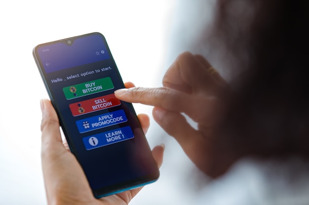 Femme tenant des smartphones et utilisant le toucher du doigt sur l'écran et sélectionnant les boutons de l'application d'achat et de vente pour le commerce d'argent numérique en bitcoin ou en crypto-monnaie.