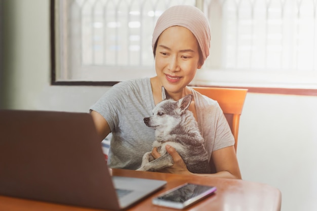 Femme tenant son chien Chihuahua tout en travaillant sur un ordinateur portable à la maison