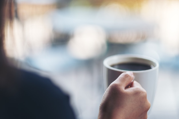 Une femme tenant une tasse blanche de café chaud avec un arrière-plan flou