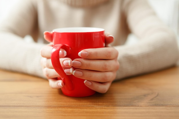 Femme tenant une tasse de boisson chaude assise à une table en bois, faible profondeur de champ.