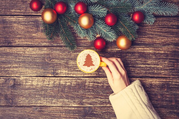 Femme tenant une tasse de café avec un arbre de Noël crème sur une table.