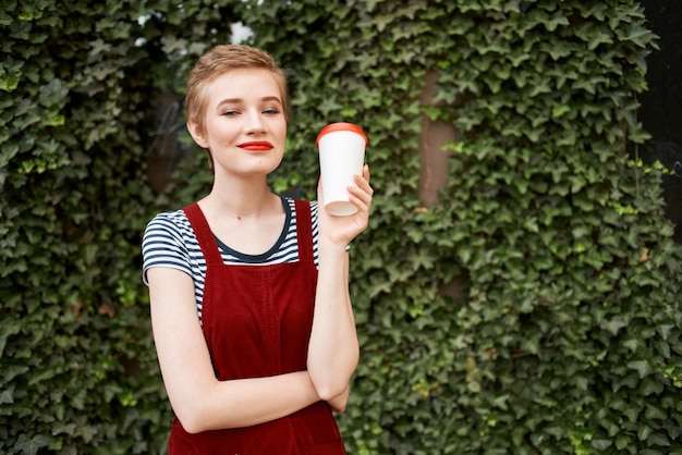 Femme tenant une tasse de café dans ses mains dans la rue près des buissons vacances d'été