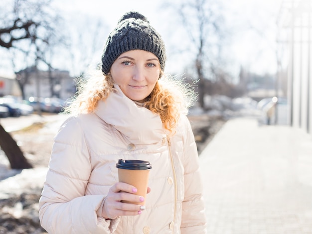 Femme tenant une tasse de café en papier brun en plein air.