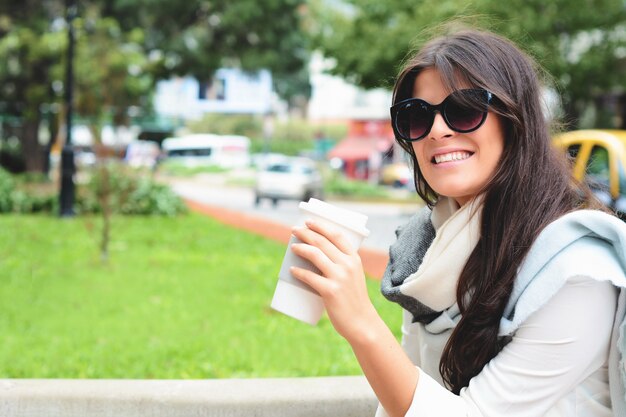 Femme tenant une tasse de café en papier dans la rue.