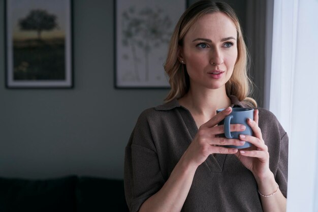 Une femme tenant une tasse de café en regardant loin de chez elle.