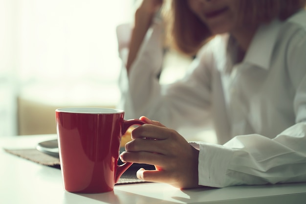 Femme tenant une tasse de café rouge le matin