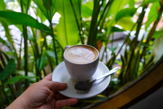 Femme tenant une tasse grise de cappuccino avec un bel art latte