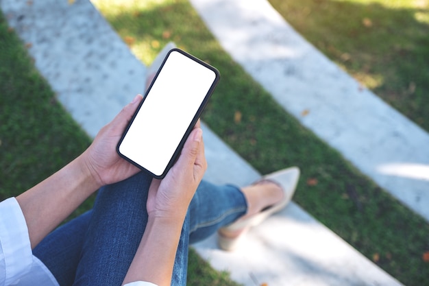 Femme tenant un téléphone mobile noir avec écran blanc vide alors qu'il était assis dans le parc