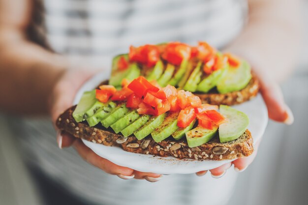 Femme tenant des toasts à l'avocat et aux tomates sur la plaque.