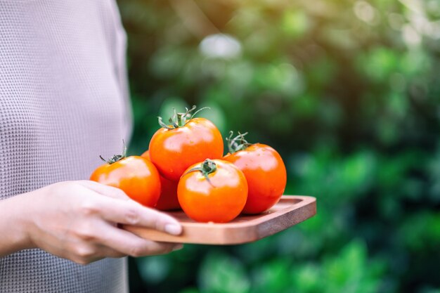 Une femme tenant des tomates fraîches dans un plateau en bois