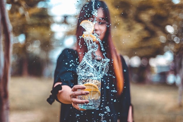 Photo une femme tenant des tranches de citron tombant dans la boisson alors qu'elle se tient à l'extérieur