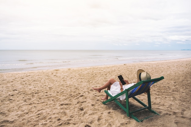 Une femme tenant et utilisant un téléphone portable en s'allongeant sur une chaise de plage