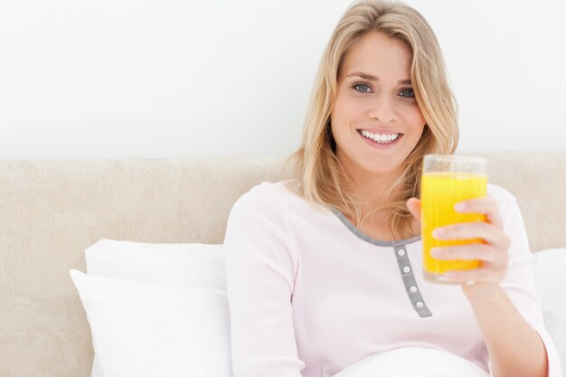 Femme tenant un verre de jus d&#39;orange en souriant et en regardant vers l&#39;avant