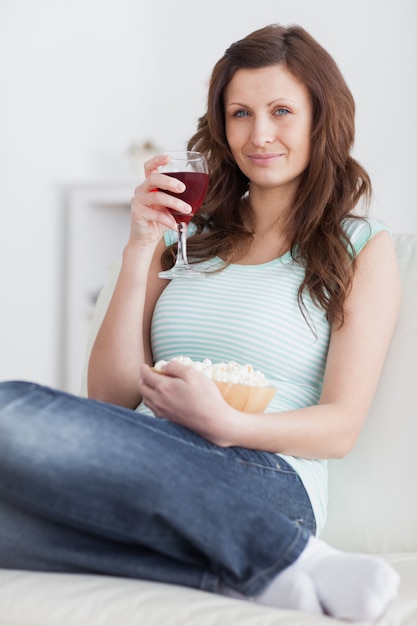 Femme tenant un verre de vin rouge et un bol de maïs soufflé