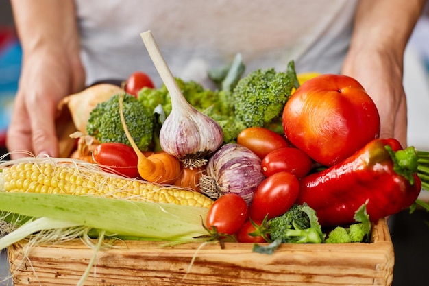 Femme tenir dans les mains une boîte en bois avec différents légumes frais de la ferme