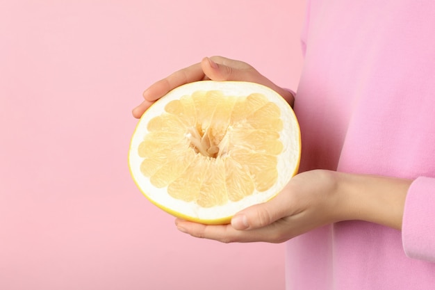 Femme tenir la moitié du pomelo sur rose, gros plan