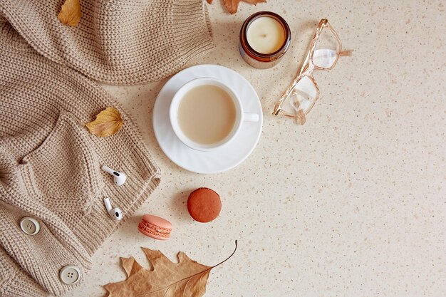 Femme tenue d'automne pull décontracté et lunettes avec casque Temps de café esthétique parmi les bougies feuilles d'automne macarons Espace de copie