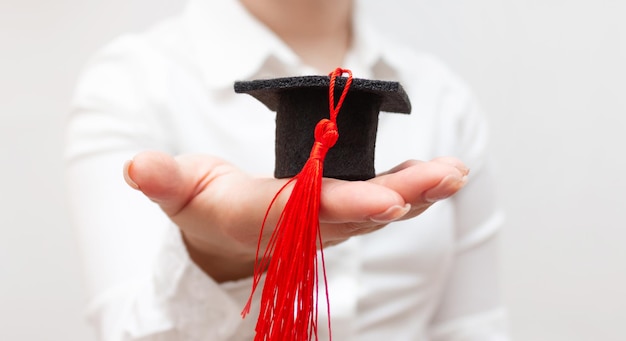 Une femme en tenue blanche tient une casquette de graduation avec un gland rouge sur la main Vue de face