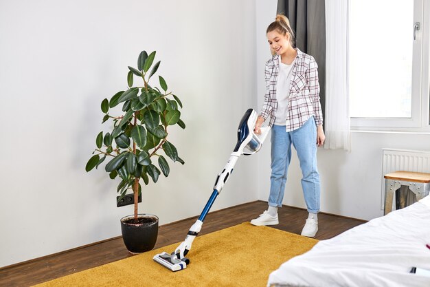 Femme en tenue décontractée aspirateur tapis jaune rangement blanc salon moderne concept d'entretien ménager