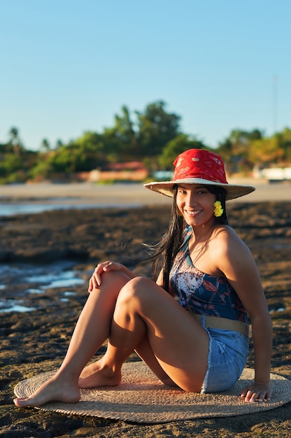 Femme en tenue d'été assis sur la rive au coucher du soleil en regardant la caméra