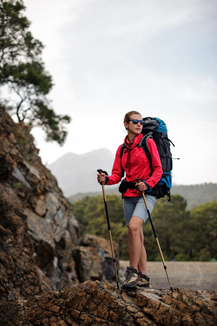 Photo femme en tenue spéciale debout avec sac à dos de randonnée et bâtons sur le rocher
