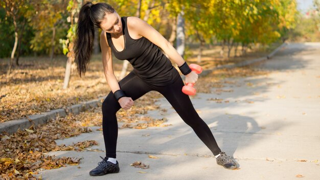 Femme en tenue de sport se penchant en avant et levant son bras sur le côté tout en travaillant avec un haltère