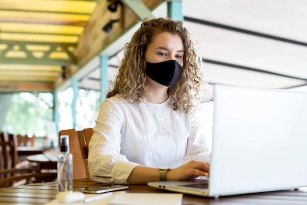 Femme à la terrasse avec masque à l'aide d'un ordinateur portable