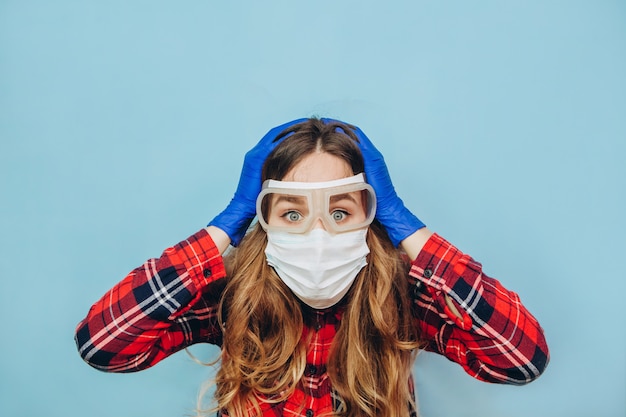 Femme terrifiée dans des lunettes de protection, un masque médical et des gants bleus. portrait de gros plan d'une femme dans un masque transparent. moyen de se protéger contre le coronavirus. Covid-2019