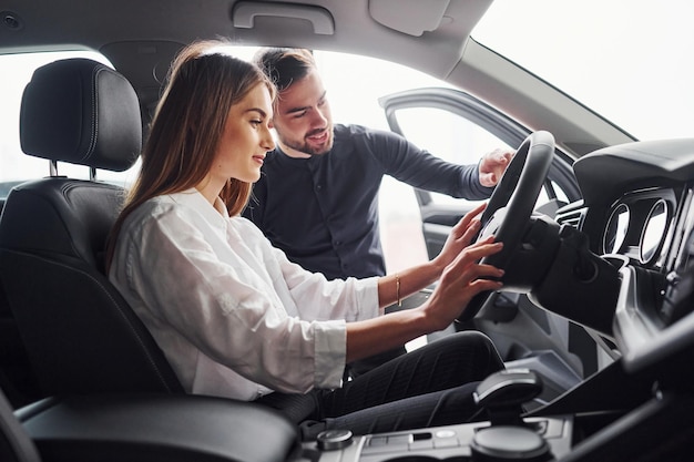 Femme testant la voiture avec l'aide d'un assistant masculin à l'intérieur dans le salon.