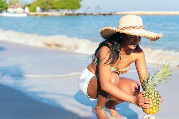 Une femme tient un ananas avec la mer en arrière-plan.