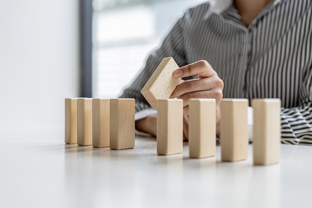 Une femme tient des blocs de bois alignés, elle saisit la pièce centrale pour les compléter, l'arrangement des blocs de bois transmet le fonctionnement de l'entreprise par une gestion efficace. Idée d'affaires.