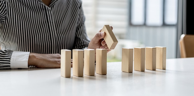 Une femme tient des blocs de bois alignés, elle saisit la pièce centrale pour les compléter, l'arrangement des blocs de bois transmet le fonctionnement de l'entreprise par une gestion efficace. Idée d'affaires.