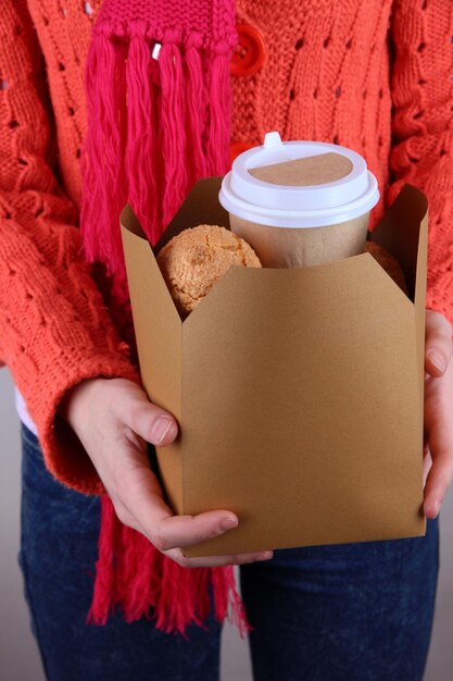 Femme tient une boîte avec du café et des biscuits sur fond gris