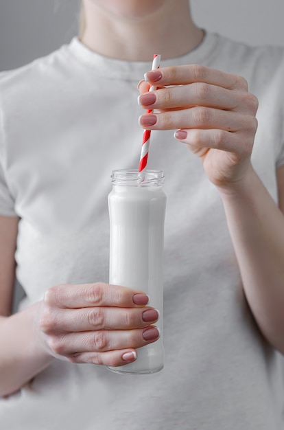 Une femme tient une bouteille en verre avec un cocktail de protéines (lait) dans un biscuit. Boire un verre avec une paille. Soins de santé