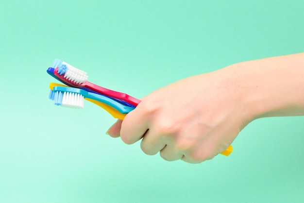 La femme tient des brosses à dents dans sa main sur un fond vert.