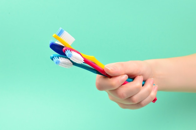 La femme tient des brosses à dents à la main sur un fond vert.