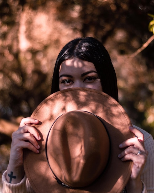 Une femme tient un chapeau devant un arbre.