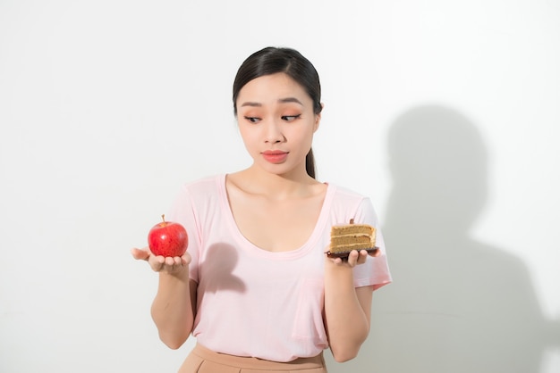 Une femme tient dans la main des gâteaux sucrés et des pommes en choisissant, essayant de résister à la tentation, de faire le bon choix diététique. Concept de gourmandise de dilemme de régime de perte de poids.