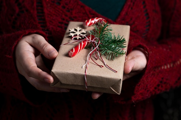 Une femme tient dans ses mains un cadeau noué d'un fil décoré d'un brin de nobilis et d'un bâton de caramel